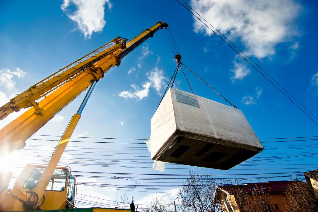 Industrial Crane operating and lifting an electric generator against sunlight and blue sky
