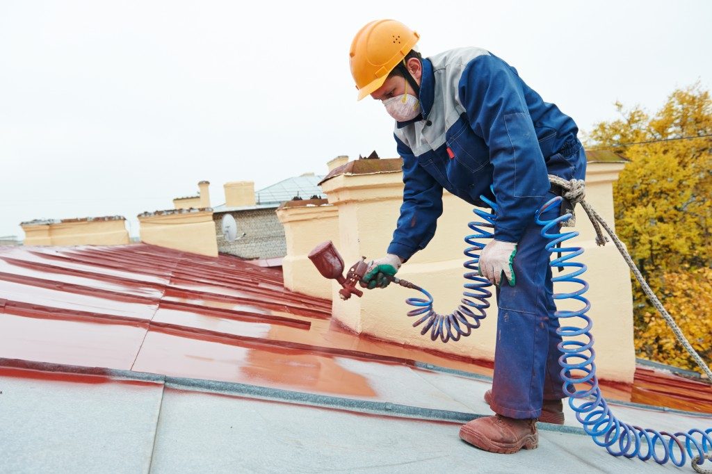 man spray painting metal sheet roofing